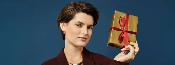 A confident young woman presents a charming gold gift box tied with a red ribbon. — Stock Photo