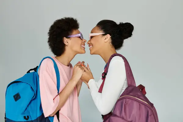 Dois amigos expressam seu vínculo com um gesto lúdico enquanto usam óculos escuros e mochilas. — Fotografia de Stock