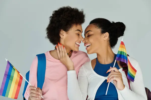 Two friends share a tender moment while holding rainbow flags, celebrating love and friendship. — Stock Photo