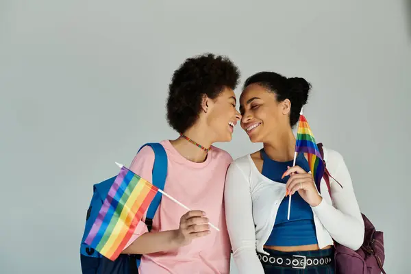 Two friends share a joyful moment holding rainbow flags, celebrating love and inclusivity. — Stock Photo