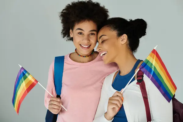 Deux filles joyeuses tiennent des drapeaux arc-en-ciel, mettant en valeur l'amitié et la fierté lors d'une célébration vibrante. — Photo de stock