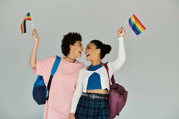 Dois amigos alegremente acenam bandeiras do arco-íris, celebrando seu orgulho e unidade em uma atmosfera brilhante. — Fotografia de Stock