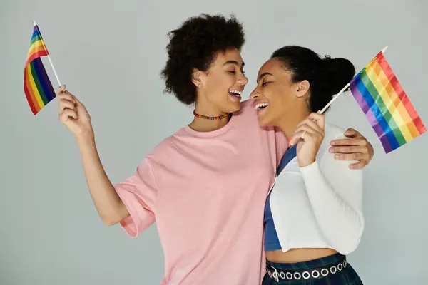 Two friends share a heartfelt moment while proudly waving rainbow flags during a celebration. — Stock Photo