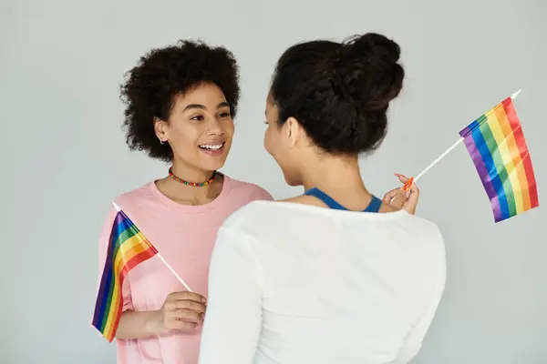 Dois amigos compartilham o riso e a alegria enquanto orgulhosamente acenam bandeiras do arco-íris em uma celebração animada. — Fotografia de Stock