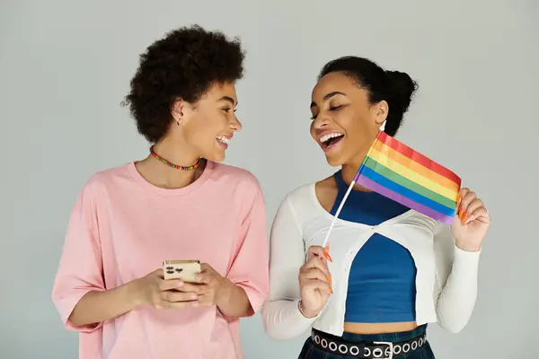 Two friends joyfully hold a rainbow flag, sharing laughter and each others company. — Stock Photo