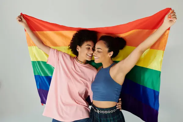 Two friends warmly embrace while holding a rainbow flag, celebrating love and diversity together. — Stock Photo