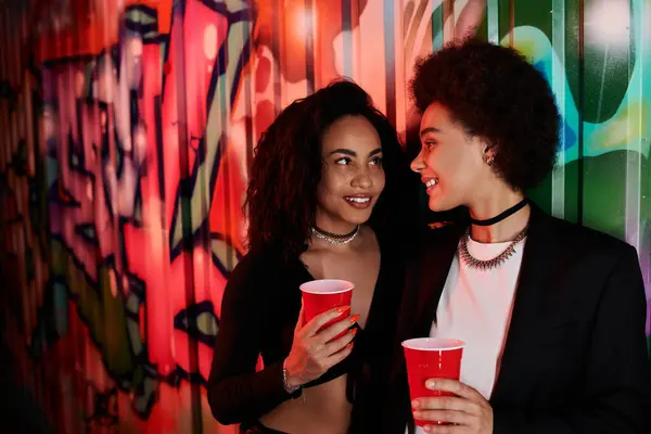 Two friends share a joyful moment together against a backdrop of vivid street art at night. — Stock Photo