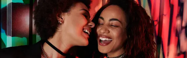 Two young women enjoy a moment of connection and laughter against a bright, artistic backdrop. — Stock Photo