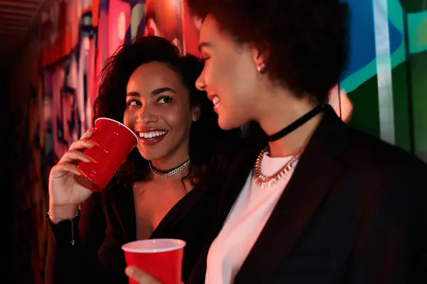 Friends share laughter and drinks in a lively urban setting, illuminated by street art. — Stock Photo