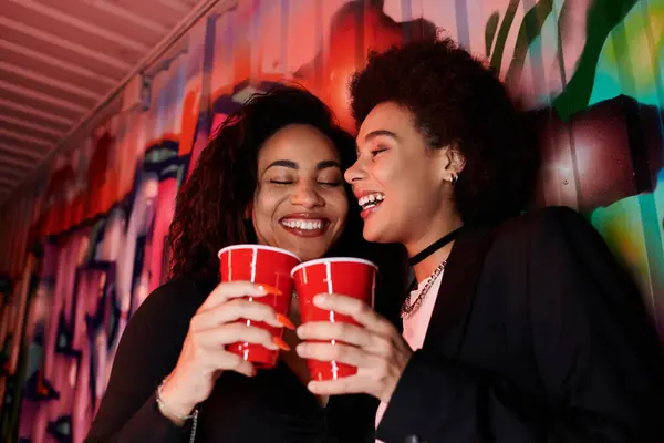 Friends celebrate together, holding red cups and laughing exuberantly in vibrant surroundings. — Stock Photo