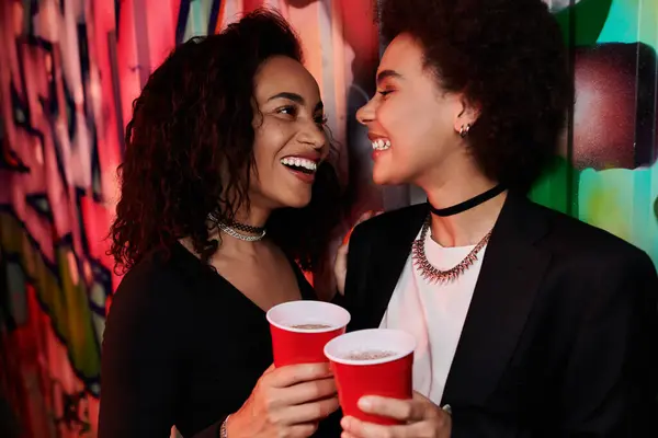 Friends share joyful moments and drinks against a colorful graffiti backdrop. — Stock Photo