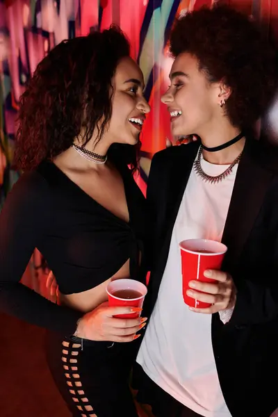 Two friends enjoy a lively moment, sharing smiles while holding drinks in a colorful setting. — Stock Photo