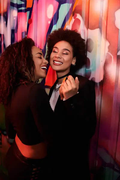 Two friends laugh and embrace, surrounded by colorful street art in an energetic atmosphere. — Stock Photo