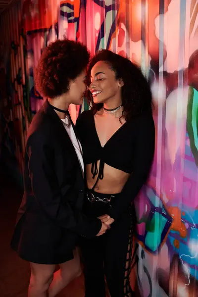 Two young women share a joyful interaction, illuminated by colorful graffiti lights. — Stock Photo