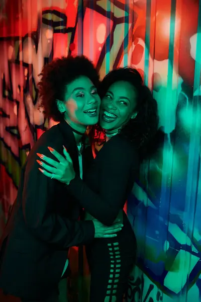 Two friends share a joyful moment, embracing each other amid colorful urban graffiti at night. — Stock Photo