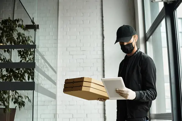 Un professionista della consegna in una maschera nera porta scatole di cibo in un ambiente ufficio moderno. — Foto stock