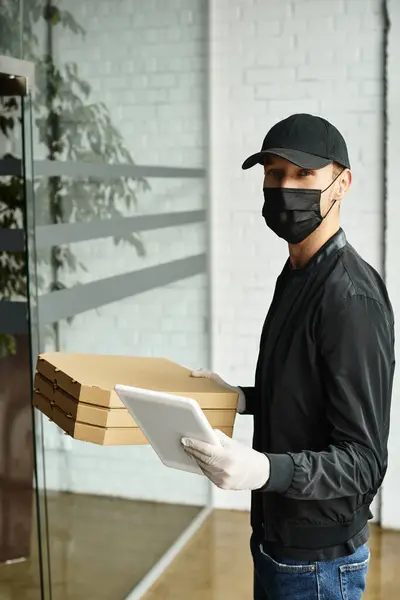 A delivery man wearing a black mask and gloves arrives with pizza boxes at an office entrance. — Stock Photo
