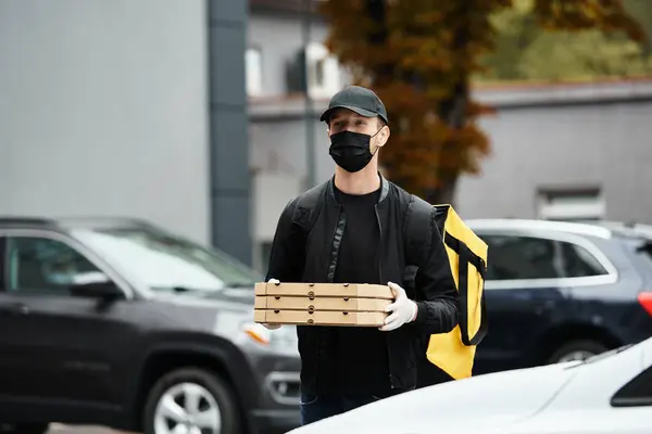 Um homem de entrega com uma máscara preta traz ordens de comida para um prédio de escritórios, garantindo uma pausa para o almoço para o pessoal. — Fotografia de Stock