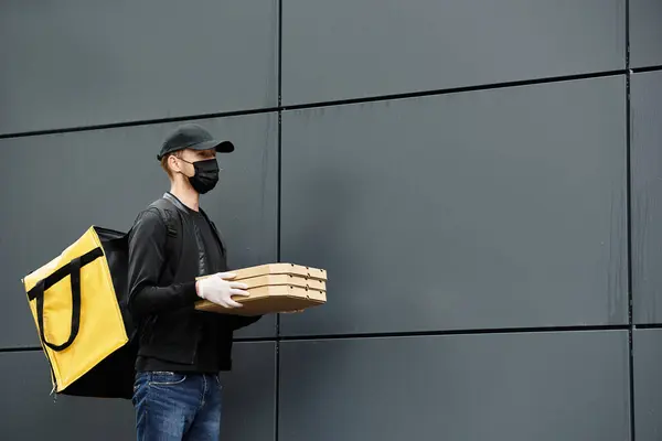 Um homem de entregas usando uma máscara médica preta traz ordens de comida para um prédio de escritórios enquanto usa luvas. — Fotografia de Stock