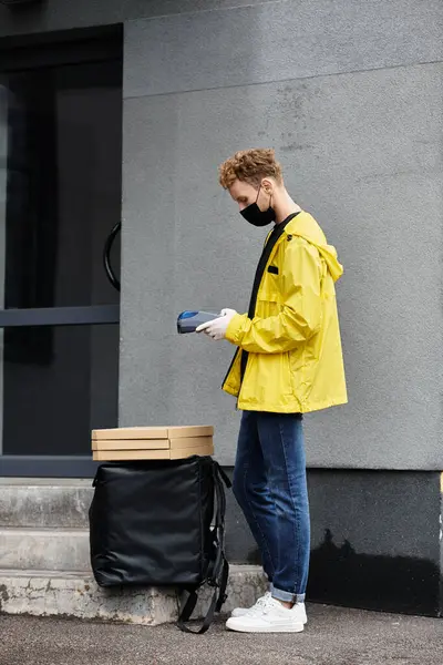 A delivery man wearing a black mask prepares to take lunch orders into a modern office environment. — Stock Photo