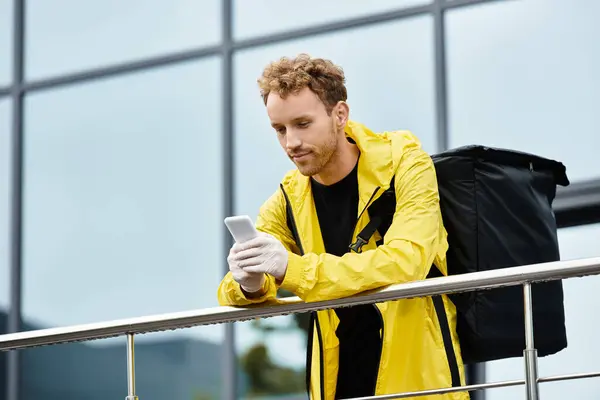 A delivery man stands outside an office building checking his phone. — Stock Photo