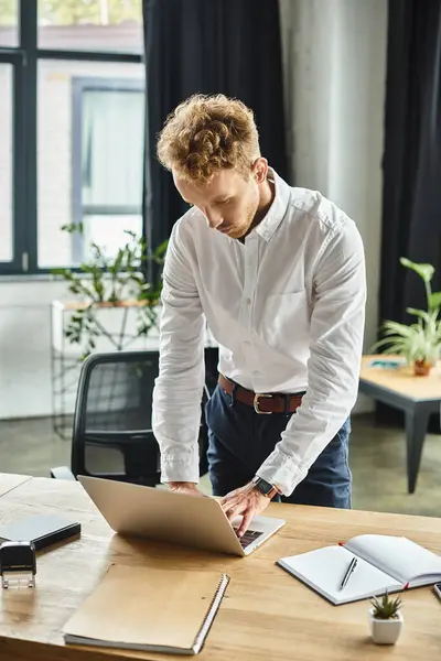 In a sleek office, a redhead businessman in a white shirt intensively works on a project at his desk. — Stock Photo
