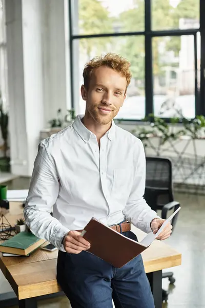 Um empresário ruivo focado analisa um projeto enquanto está em sua mesa em um ambiente de escritório vibrante. — Fotografia de Stock