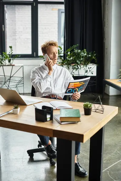 Um empresário focado com cabelo vermelho examina um relatório do projeto e discute detalhes sobre uma chamada telefônica no trabalho. — Fotografia de Stock