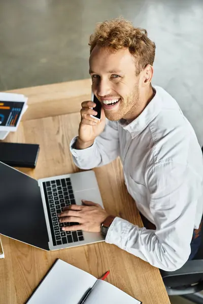 A redheaded businessman in a white shirt is actively discussing his project on the phone while working at his desk. — Stock Photo