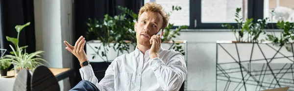 A focused redheaded professional engages in a project discussion over the phone in his sleek office. — Stock Photo