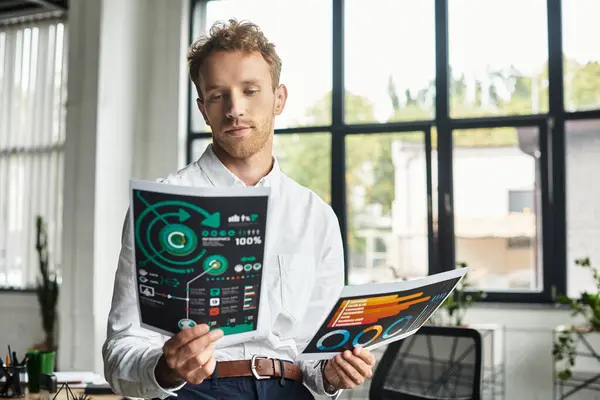 A focused businessman with red hair analyzes project reports in a contemporary office filled with natural light. — Stock Photo