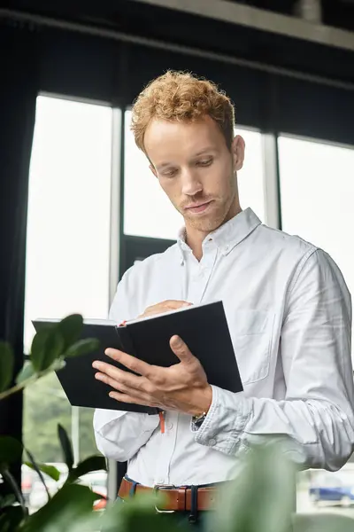 Ein rothaariger Geschäftsmann in weißem Hemd analysiert ein Projekt in seinem stilvollen, modernen Arbeitsplatz gründlich. — Stockfoto