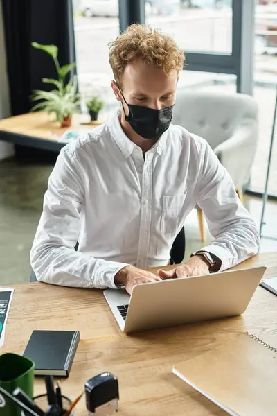 In a contemporary office, a redhead in a white shirt focuses intently on his project using a laptop. — Stock Photo