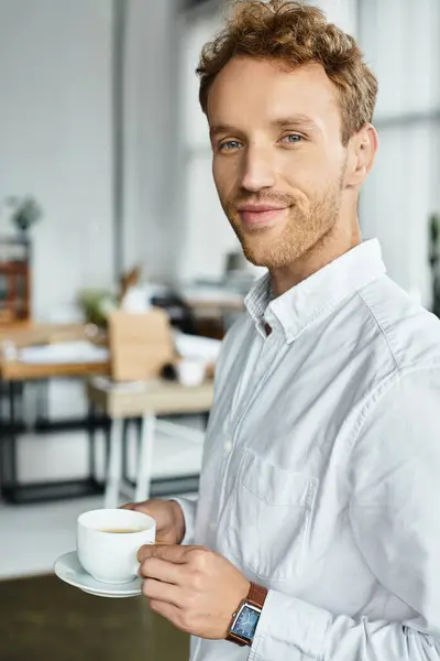 A redhead businessman holds a coffee cup while working on a project in a contemporary office environment. — Stock Photo