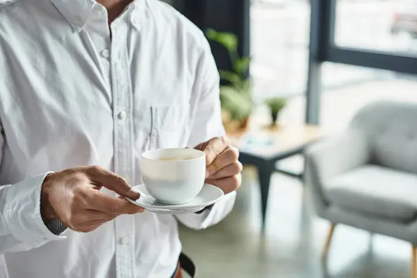 A businessman in a white shirt holds a cup of coffee while concentrating on his project in a modern office. — Stock Photo