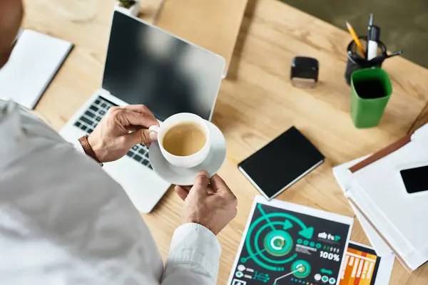 In un ufficio elegante e moderno, un uomo d'affari valuta i documenti di progetto mentre assapora il suo caffè. — Foto stock