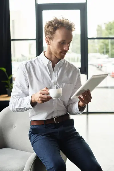 A professional redhead reviews project details on a tablet while enjoying a coffee in a sleek office. — Stock Photo