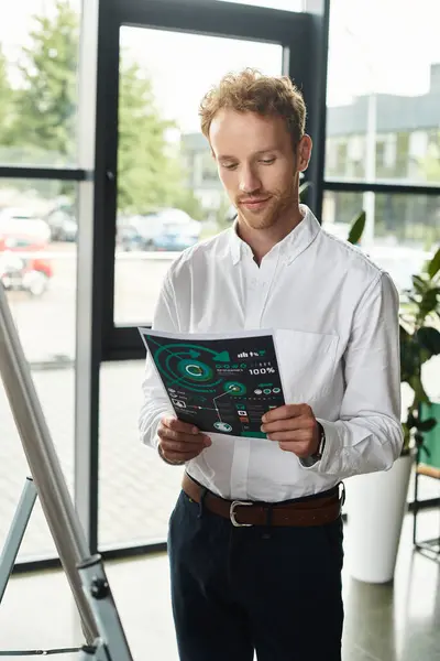 A dedicated businessman with red hair studies project materials in a contemporary office setting. — Stock Photo
