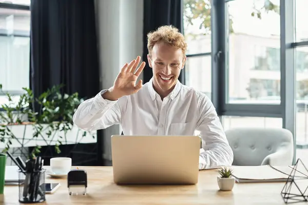 The redhead businessman in a white shirt smiles and waves while working on a project in a modern office. — Stock Photo