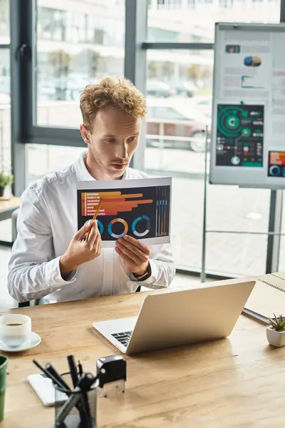 A redheaded professional in a white shirt examines project graphs while seated at a modern workspace. — Stock Photo