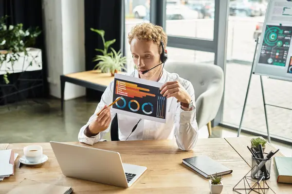 Un empresario pelirrojo revisa su proyecto mientras se comunica a través de un auricular en una oficina contemporánea. - foto de stock