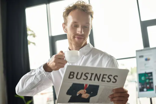 A professional man reads a business article with a coffee cup in hand, immersed in his work at a stylish office. — Stock Photo