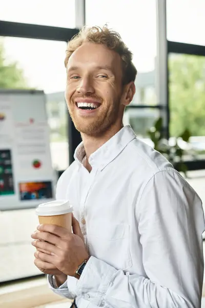 A professional redhead enthusiastically holds a coffee cup while developing ideas in a contemporary workspace. — Stock Photo