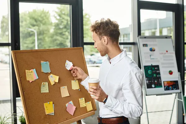 A redhead businessman in a white shirt analyzes project notes while holding a coffee cup in a sleek office space. — Stock Photo