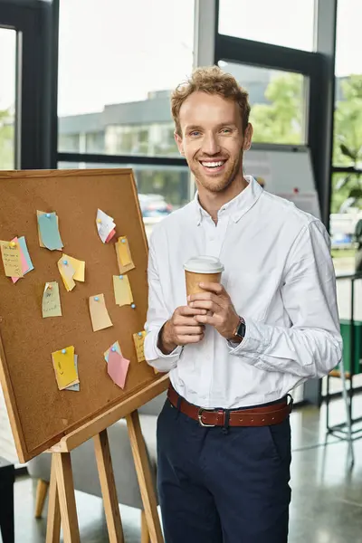 A joyful redhead in a white shirt holds a coffee cup while brainstorming in a contemporary office. — Stock Photo