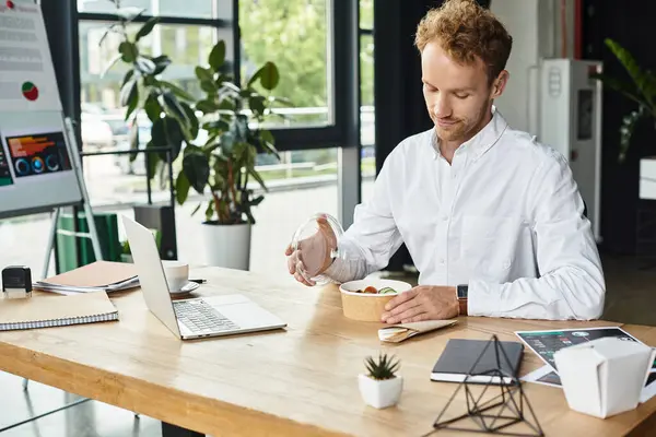 A redheaded professional works diligently on a project while enjoying a light lunch in a stylish office. — Stock Photo