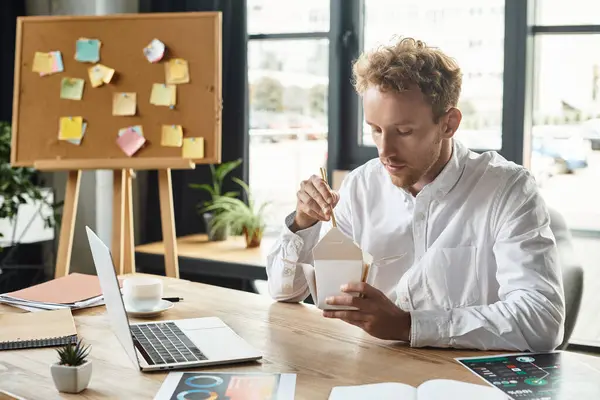 A focused businessman with red hair enjoys a meal while collaborating on a project in a stylish office. — Stock Photo