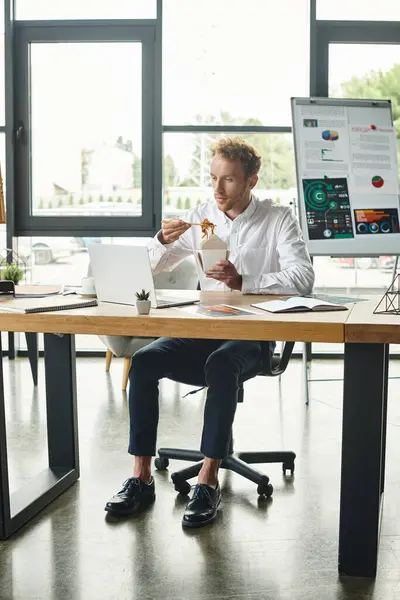 Um empresário ruivo em uma camisa branca almoça enquanto se concentra em seu projeto em um escritório moderno e brilhante. — Fotografia de Stock