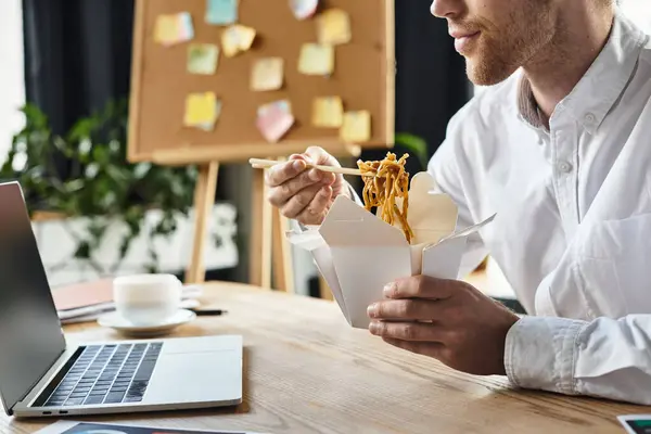 Професіонал у білій сорочці зосереджується на роботі, смакуючи смачну їжу в сучасному робочому просторі. — стокове фото
