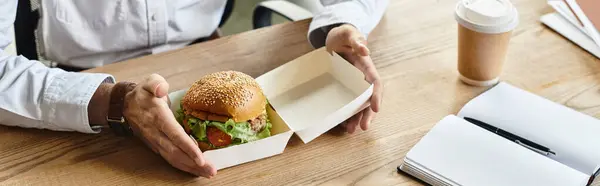 Profi im weißen Hemd nimmt sich einen Moment Zeit, um einen Burger zu genießen, während er an einem Projekt arbeitet. — Stockfoto